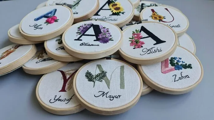 Creative embroidered letters with floral designs on fabric in embroidery hoops.