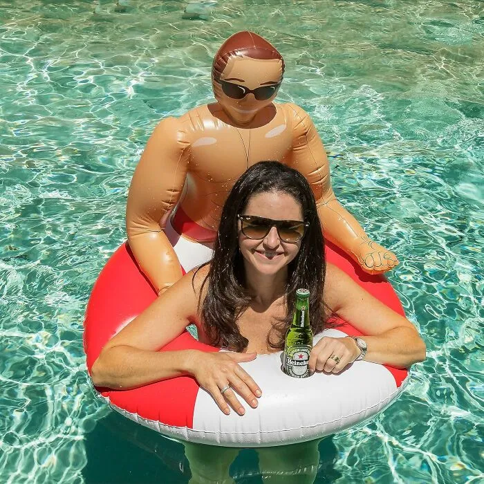 Woman in a pool with inflatable float holding a beer, smiling, enjoying leisure under the sun.