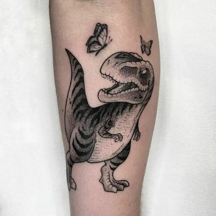 Dinosaur tattoo with butterflies on forearm, showcasing cool and creative design.