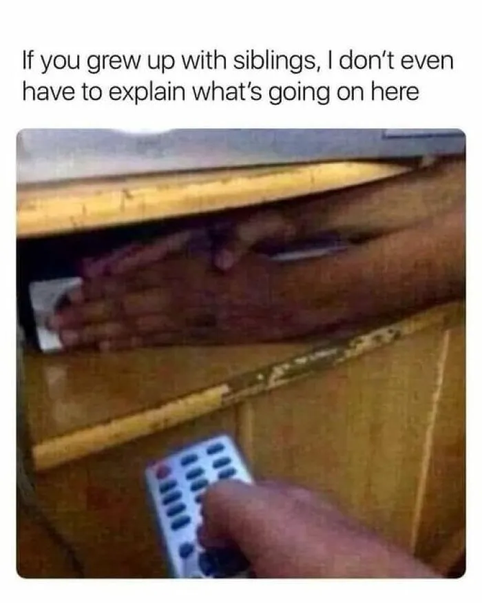 Hands hiding under a table while another hand holds a remote, capturing a nostalgic '90s sibling moment.