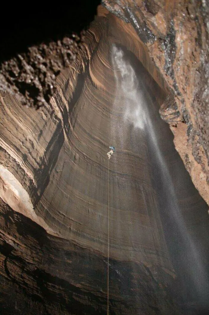 Person rappelling down a massive cave wall with mist, illustrating extreme heights that trigger megalophobia fear.