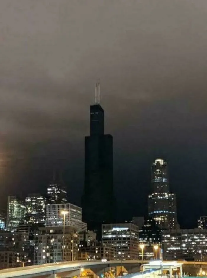 Nighttime cityscape featuring a towering skyscraper that evokes megalophobia with its immense dark silhouette.