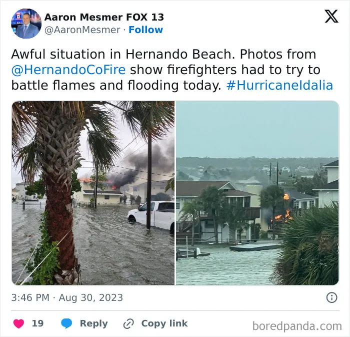 Flooded street with a burning house and firefighters battling flames during severe weather and natural disaster conditions.
