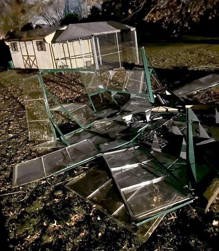 Damaged glass panels scattered on the ground near a backyard shed during nighttime after a severe weather event.