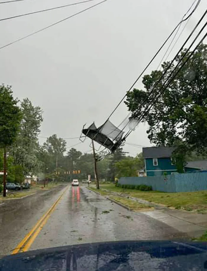 Power lines twisted above a rainy street with a trampoline tangled in the wires, showing nature’s wild impact on urban areas.