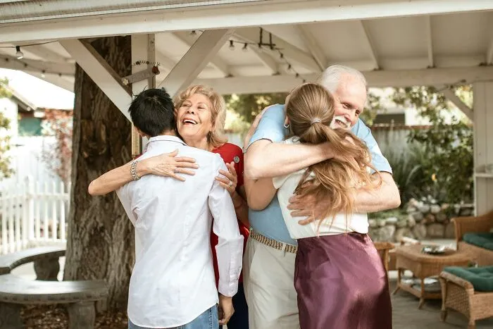 Two elderly people joyfully hugging younger family members, showing the appreciation of meaningful connections after getting older.
