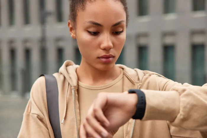 Young woman appreciating time and reflection while checking her watch outdoors in an urban setting.