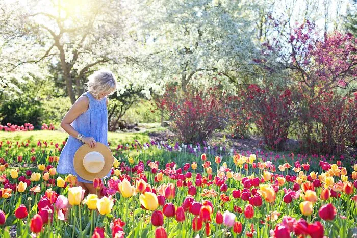 Woman in a blue dress appreciating colorful tulips in a sunny garden, reflecting on things people appreciate after getting older