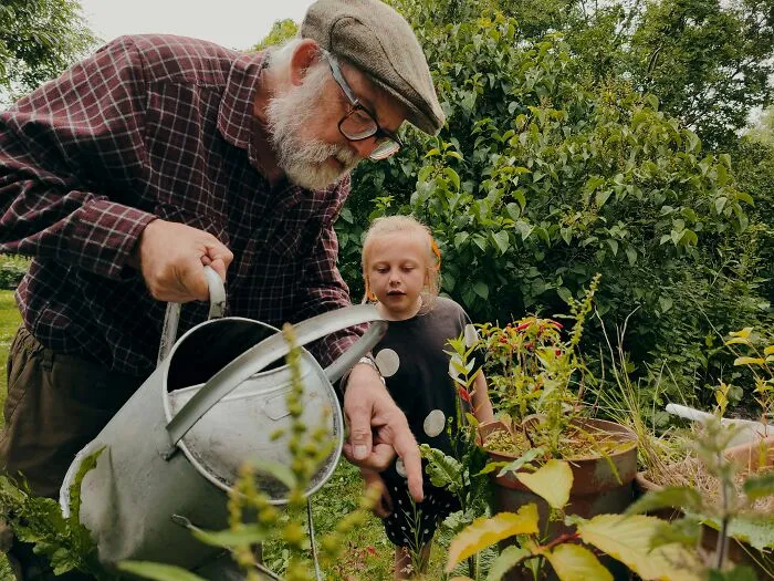Elderly man watering plants in a garden with a young girl, illustrating appreciation for nature outdoors as people get older