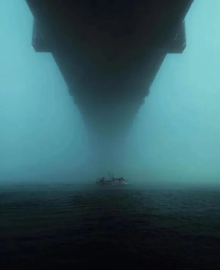 Barco pequeño bajo una estructura extremadamente grande y oscura que crea una atmósfera aterradora y de gran escala.