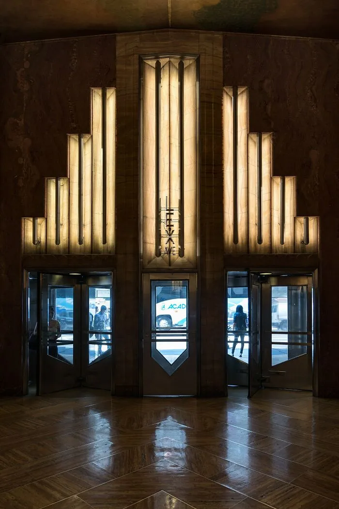 Art Deco doors with intricate illuminated geometric patterns at an iconic location entrance with reflective flooring and glass panels.