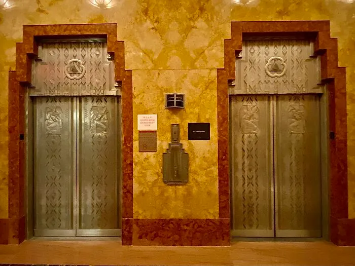 Intricate Art Deco doors with geometric patterns and bronze framing in an iconic vintage building elevator lobby.