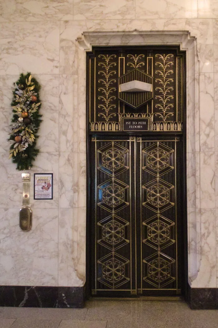 Intricate black and gold Art Deco doors with geometric floral patterns in a marble-walled iconic location interior.