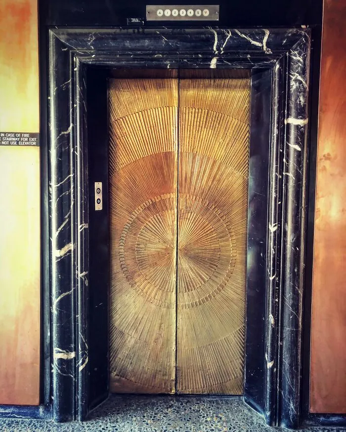 Intricate Art Deco elevator doors with sunburst design framed by black and white marble in an iconic location.