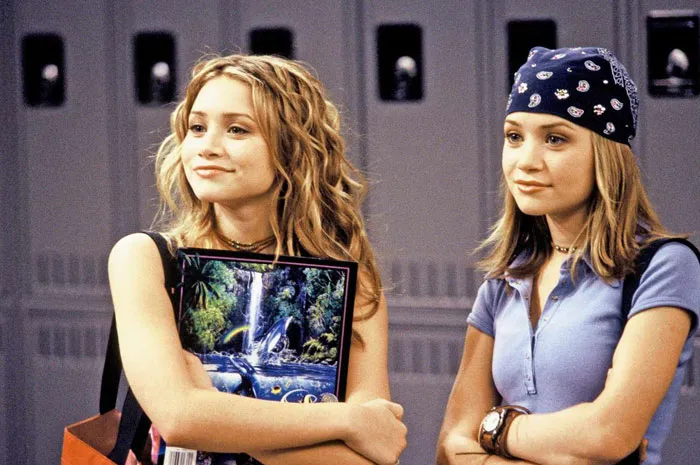 Two girls standing in front of lockers, one holding a colorful folder, representing iconic duos.