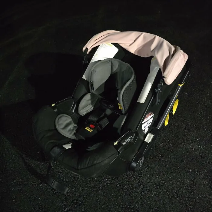 A found baby car seat, discovered during dumpster diving, rests on dark pavement.