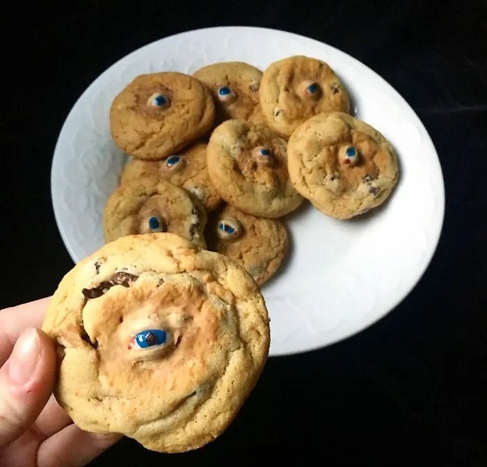 Halloween snacks featuring cookies with edible eyeballs on a white plate against a dark background.