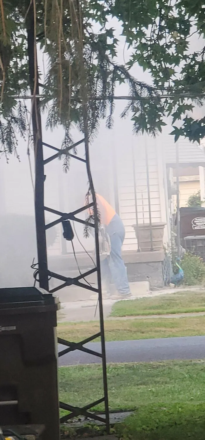 Worker blatantly ignoring safety protocol while using a power tool surrounded by dust and debris outside a residential home.