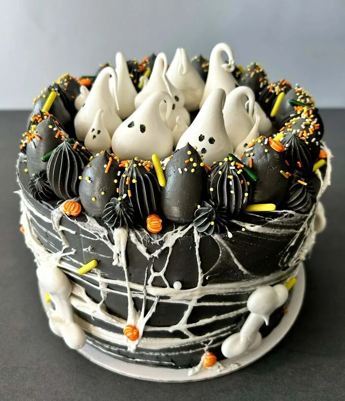 Halloween snacks featuring a black frosted cake topped with ghost-shaped meringues and colorful sprinkles.