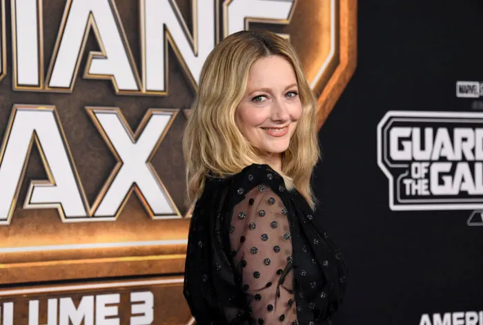 A B list celebrity, Judy Greer, is smiling while posing at the red carpet premiere of "Guardians of the Galaxy Vol. 3," wearing a black polka dot dress with a movie-themed backdrop behind her.