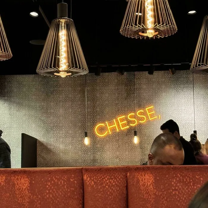 Neon sign with a misspelled word "CHESSE" causing mildly infuriating irritation in a dimly lit restaurant setting.