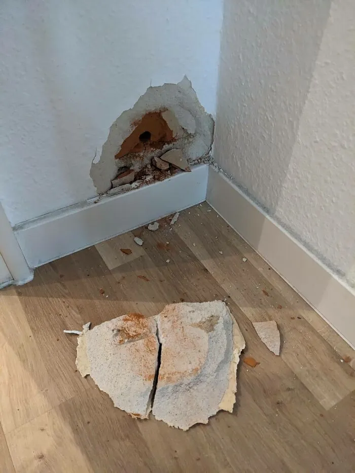 Wall damage from failed home improvement, featuring a hole and fallen plaster on the floor.