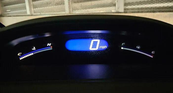 Car dashboard displaying 0 mph, showing fuel gauge almost empty; a mildly infuriating situation for drivers.