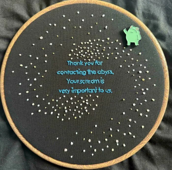 Embroidery hoop with starry pattern and blue stitched text on black fabric, showcasing unique embroidery design.