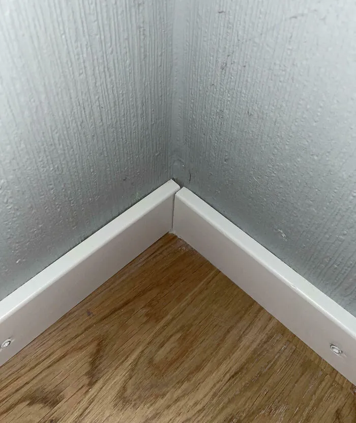 Misaligned corner baseboards showcasing a home improvement fail on wooden flooring.
