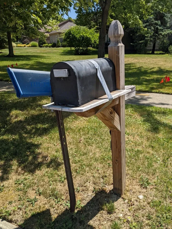 A tilted mailbox on a wooden post with duct tape, illustrating a home improvement fail.