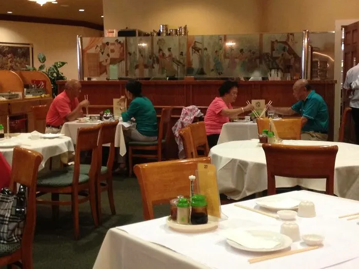 Doppelgangers dining at adjacent tables in a restaurant, wearing matching pink and teal outfits.