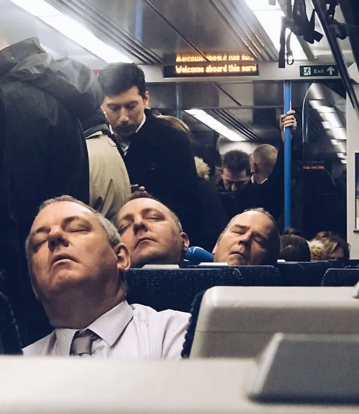 Three men asleep on a train, appearing as uncanny doppelgangers in a glitch-like moment.