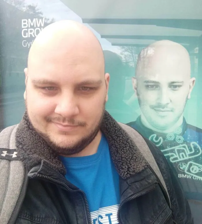 Bald man standing by a poster with his uncanny doppelganger near BMW Group sign, illustrating a Matrix glitch.