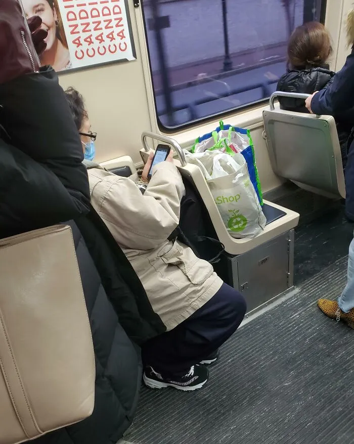 Public transport passenger occupies seat with bags, using phone.
