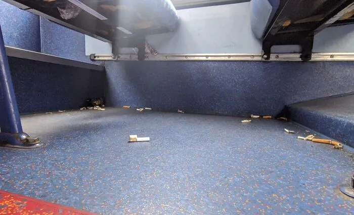 Dirty public transport floor littered with cigarette butts, showcasing infuriating passenger behavior.