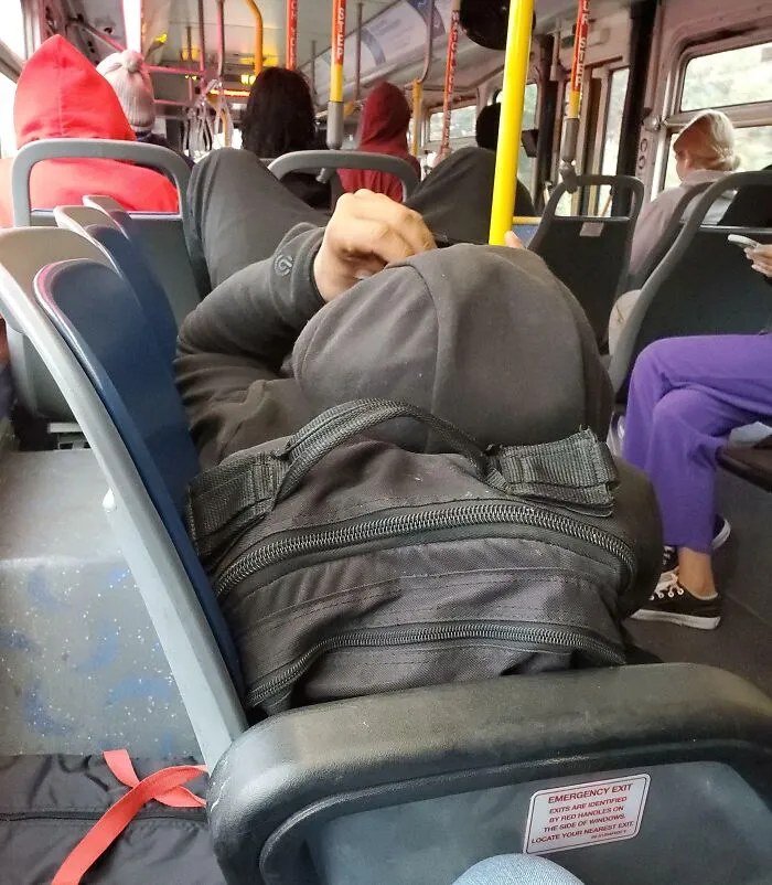 Person lying down across bus seats, blocking others, illustrating public transport passenger behavior.