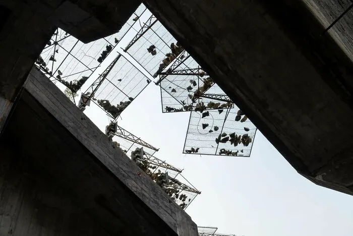 View looking up at dark concrete buildings with hanging cages of shoes, evoking evil aura supervillain headquarters vibe.