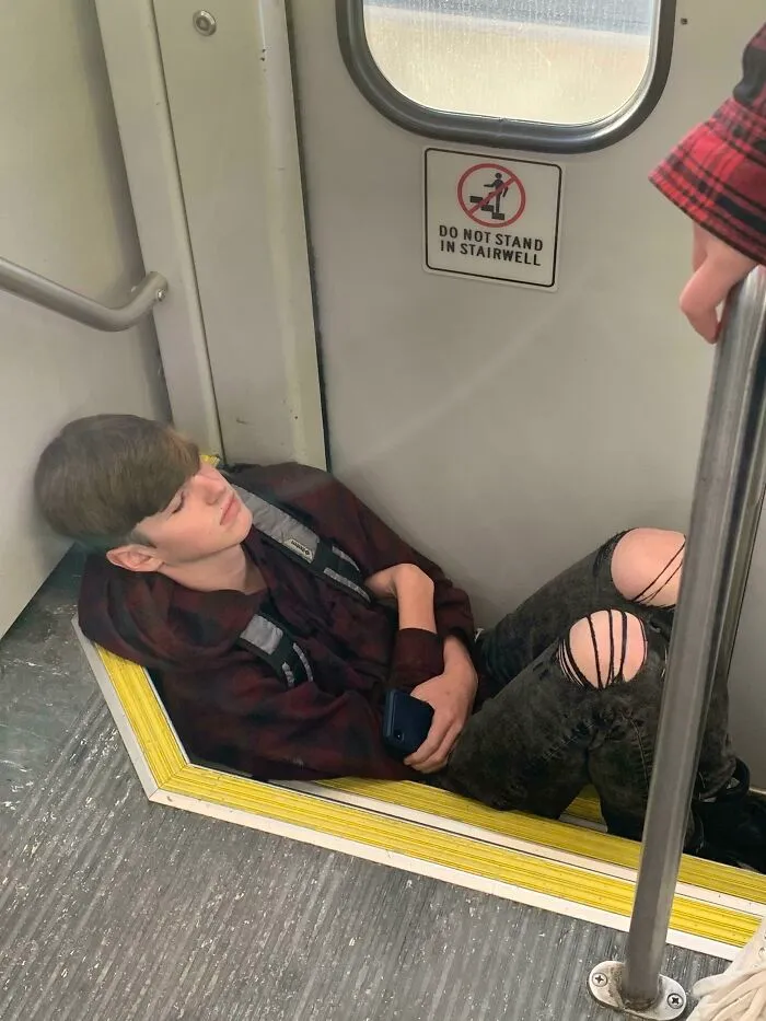 Passenger sitting on train stairs despite warning sign, showcasing public transport behavior.