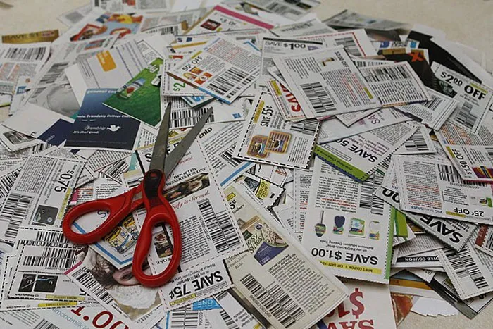 Red scissors on a pile of coupons depicting frugal choices with various savings offers.