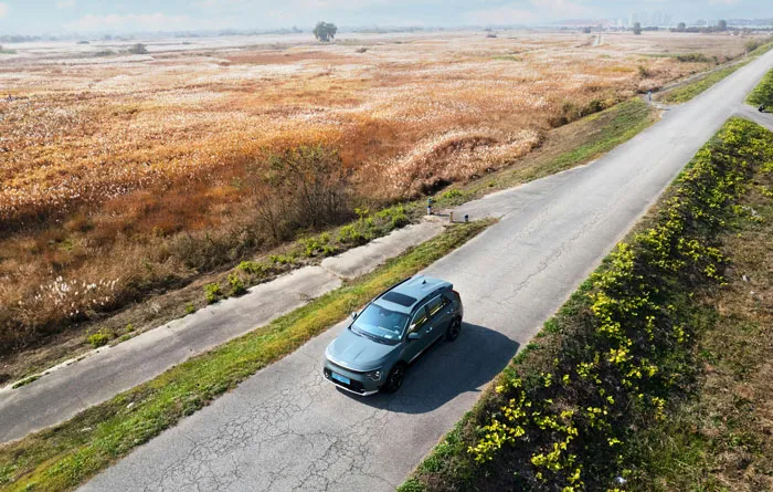 Aerial view of a frugal choice: a fuel-efficient car driving on a rural road surrounded by fields.