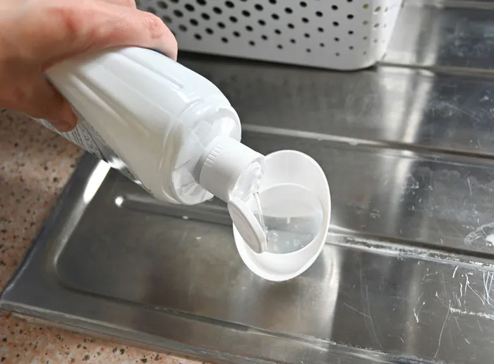Pouring liquid cleaner into cap for frugal cleaning choice in kitchen sink.