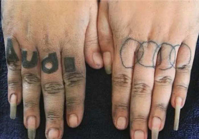 Epic tattoo fail with "Audi" text and uneven circles on fingers.