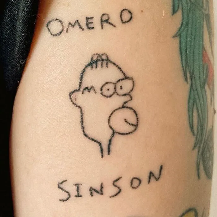 Epic tattoo fail of a poorly drawn character with misspelled names "Omerd" and "Sinson" on the skin.