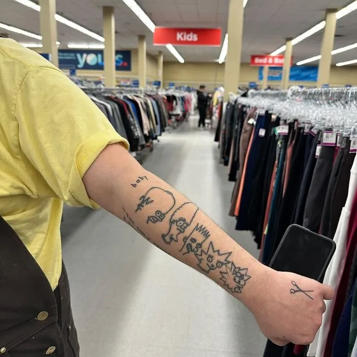 Arm with tattoo fail showing cartoon characters in a clothing store aisle.