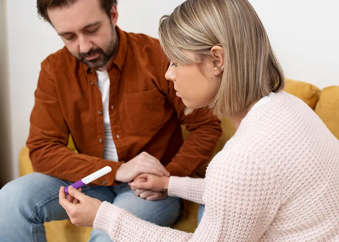 A couple sitting on a sofa, looking at a pregnancy test, appearing concerned.