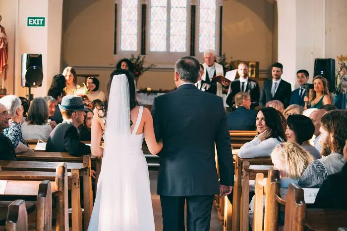Bride walking down the aisle with her father at a wedding ceremony, guests seated in a decorated church.