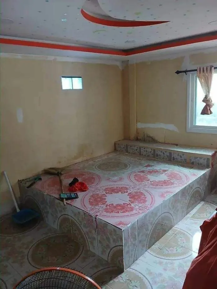 Elevated tiled bed platform in a room with cleaning tools, showcasing quirky engineer design choices.