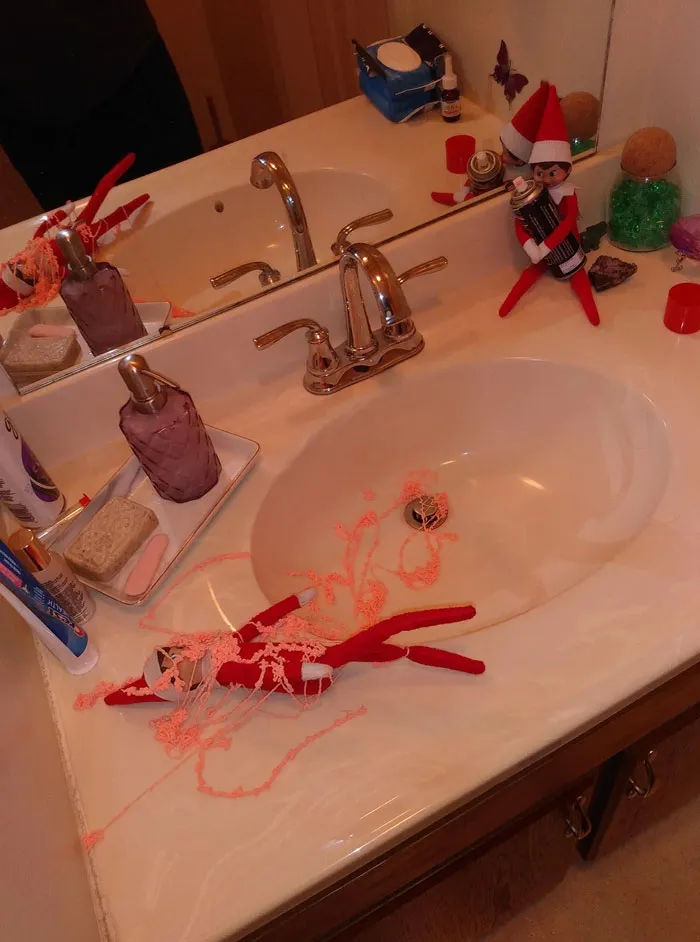 Elf On The Shelf idea with one elf spraying silly string and another covered in pink silly string on bathroom counter.