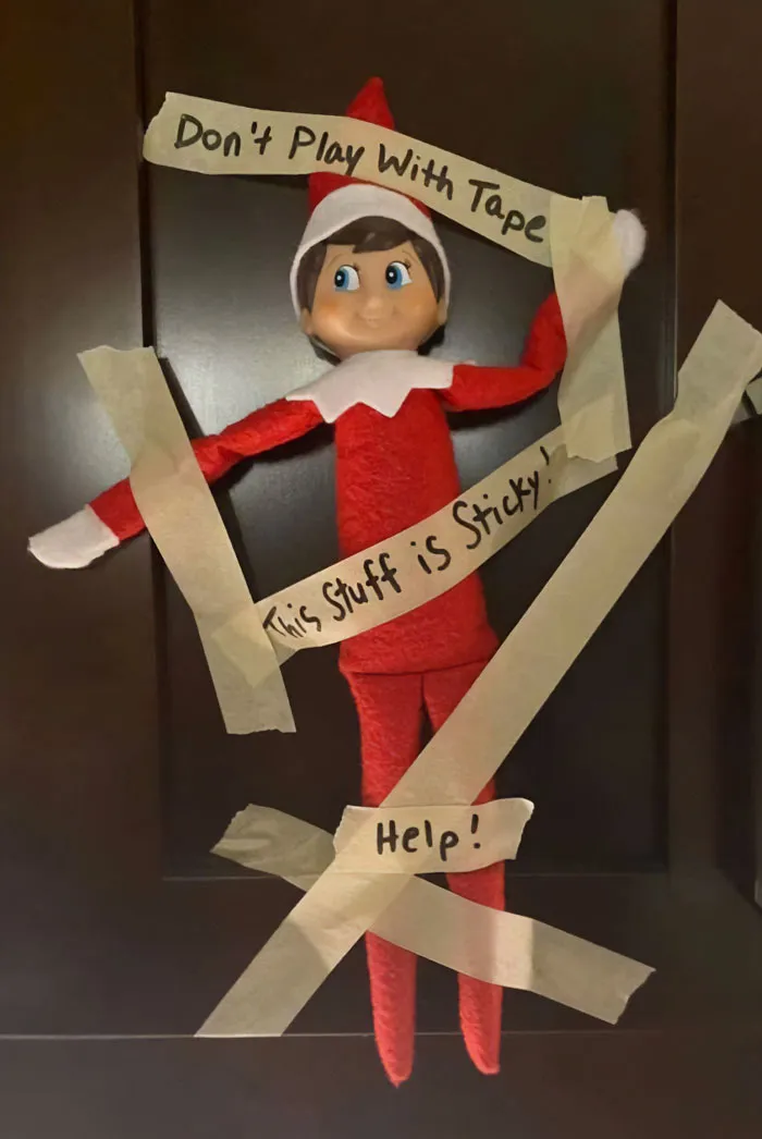Elf On The Shelf taped to door with notes saying Don't Play With Tape, This Stuff is Sticky, and Help in mischievous setup