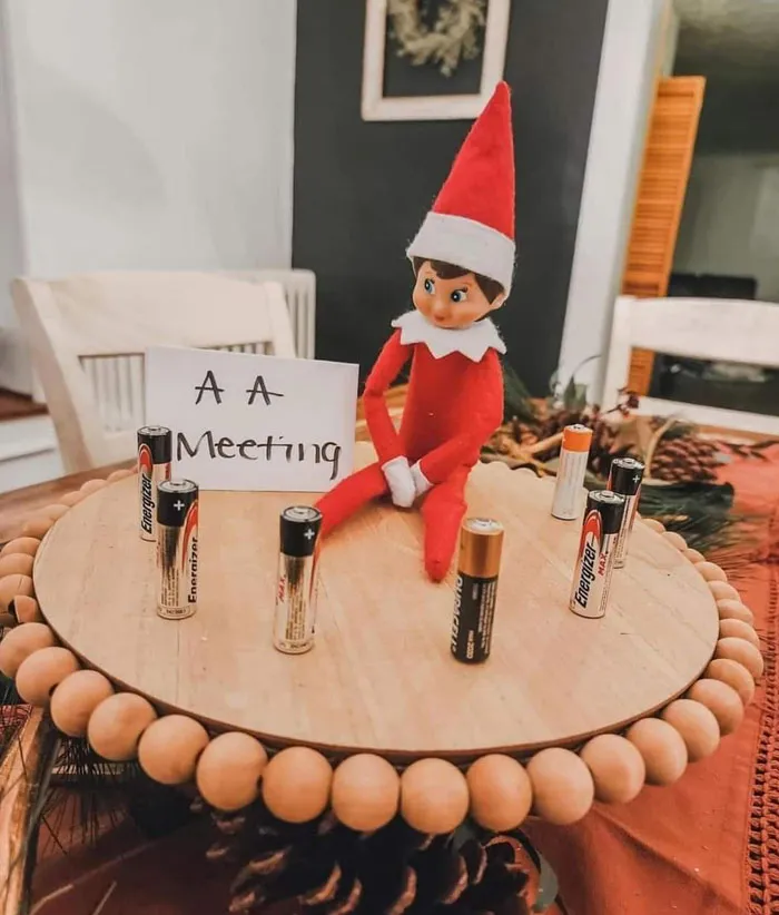 Elf On The Shelf attending a playful AA meeting surrounded by AA batteries for a clever mischief idea.